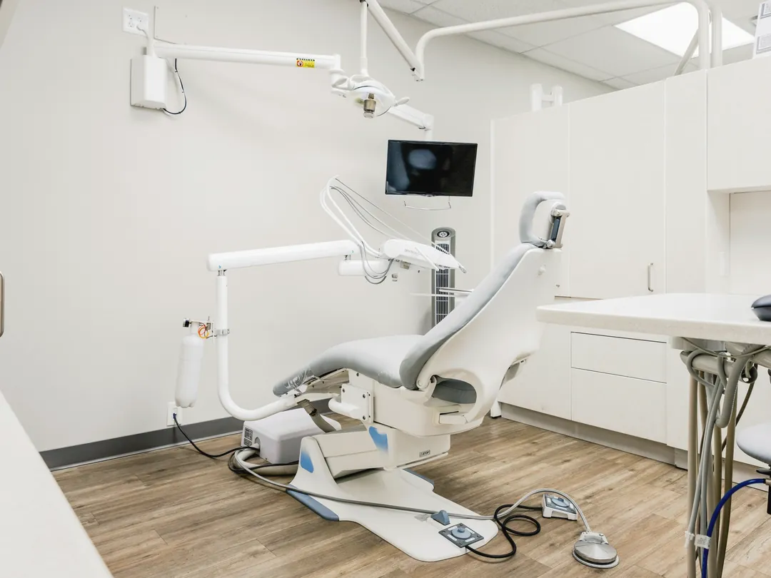 Sala de atención dental luminosa con sillón, lámpara y piso de madera.