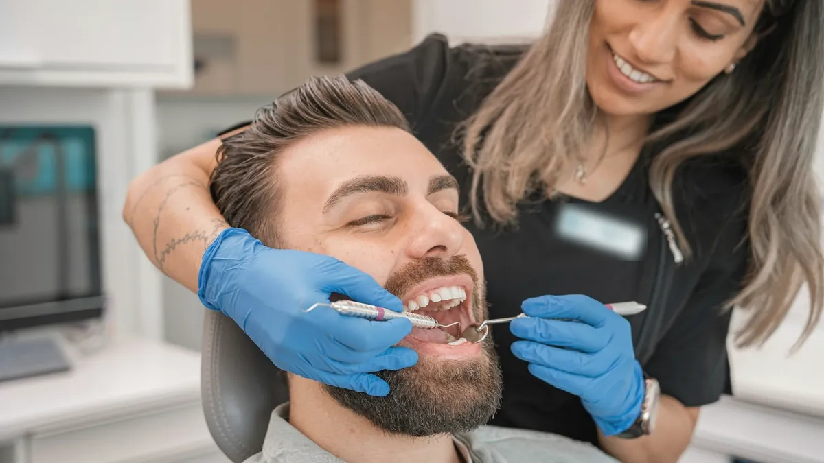 Dentista revisando la boca de un paciente sonriente.